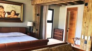 Une chambre à coucher avec un grand lit, un plafond en bois, une table de chevet, une lampe, une commode et une fenêtre avec des rideaux.