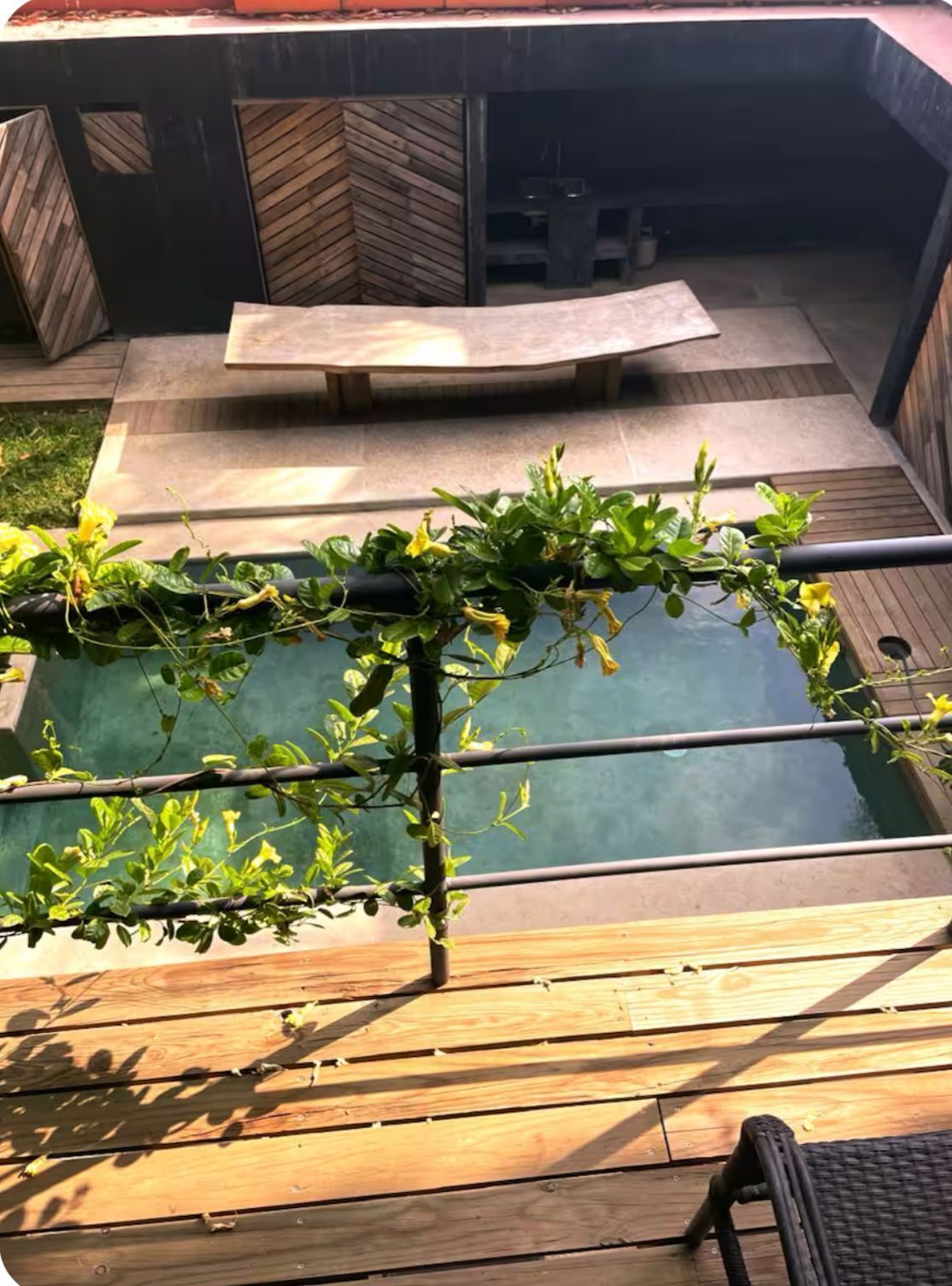 Une terrasse en bois avec une piscine, entourée d’une clôture en bois et d’un mur de pierres.