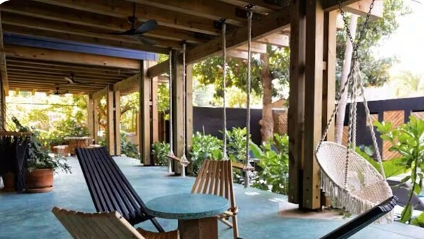 Un espace extérieur abrité, aménagé avec du mobilier en bois, notamment des fauteuils et une table, et entouré de verdure.