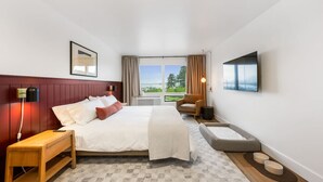 A modern hotel room with a large bed, a desk, a chair, a TV, and a view of the outdoors. - Modern Harbor Stay | Steps to Tours & Eats (Juneau)