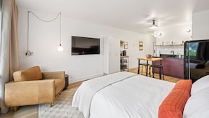 A modern hotel room with a bed, a sofa, a TV, a kitchenette, and a dining area. - Harbor Hub Retreat | Walk to Tours & Dining (Juneau)