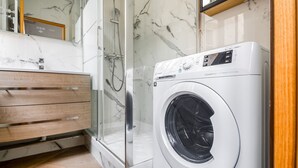 A modern bathroom with a glass shower enclosure, a wooden vanity, and a front-loading washing machine. - Blueground | Sainte-Avoye, view, nr Le Marais (Paris)