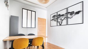 A modern dining area with a wooden table and two yellow chairs, a window with blinds, and a wall-mounted artwork of a tree. - Blueground | Sainte-Avoye, view, nr Le Marais (Paris)
