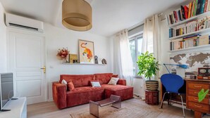 A living room with a red sofa, a coffee table, a bookshelf, a desk, and a potted plant. - LE CACTUS - Gorge de loup apartment (Lyon)