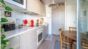 A modern kitchen with white cabinets, a built-in oven, and a dining area with a wooden table and chairs. - LE CACTUS - Gorge de loup apartment (Lyon)