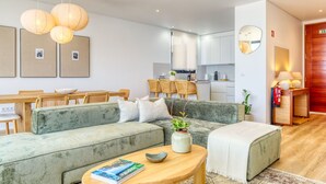 A modern living room with a green sofa, a wooden coffee table, and a dining area with a wooden table and chairs. - Villa Arco-Iris, a Home in Madeira (Arco da Calheta)