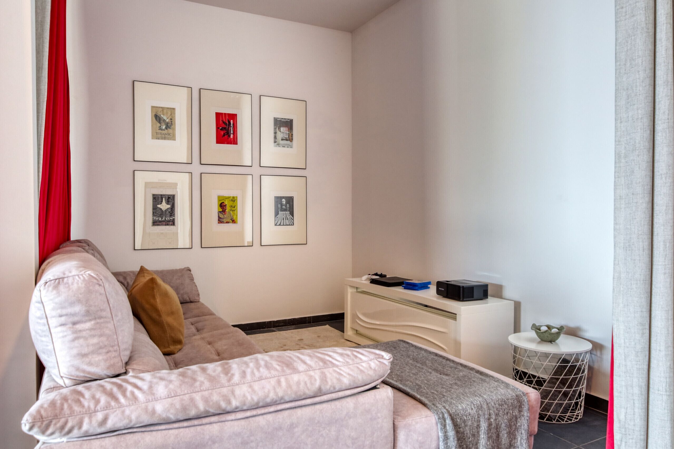 Una sala de estar moderna con un sofá, cuadros enmarcados en la pared, una mesita auxiliar y una cortina roja.