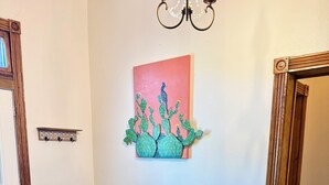 A room with a blue sofa, a wooden floor, a patterned rug, a painting of cacti, and a chandelier. - Charming Historical 4BR Home in Central Del Rio (Del Rio)