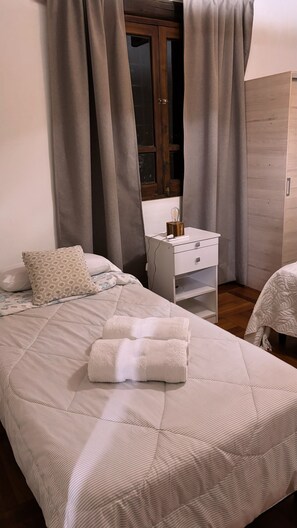 A neatly made bed with a folded white towel, a bedside table with a lamp and a remote control, and a wooden wardrobe in a well-lit room. - CASA SANTA FE HOUSE (Luján de Cuyo)