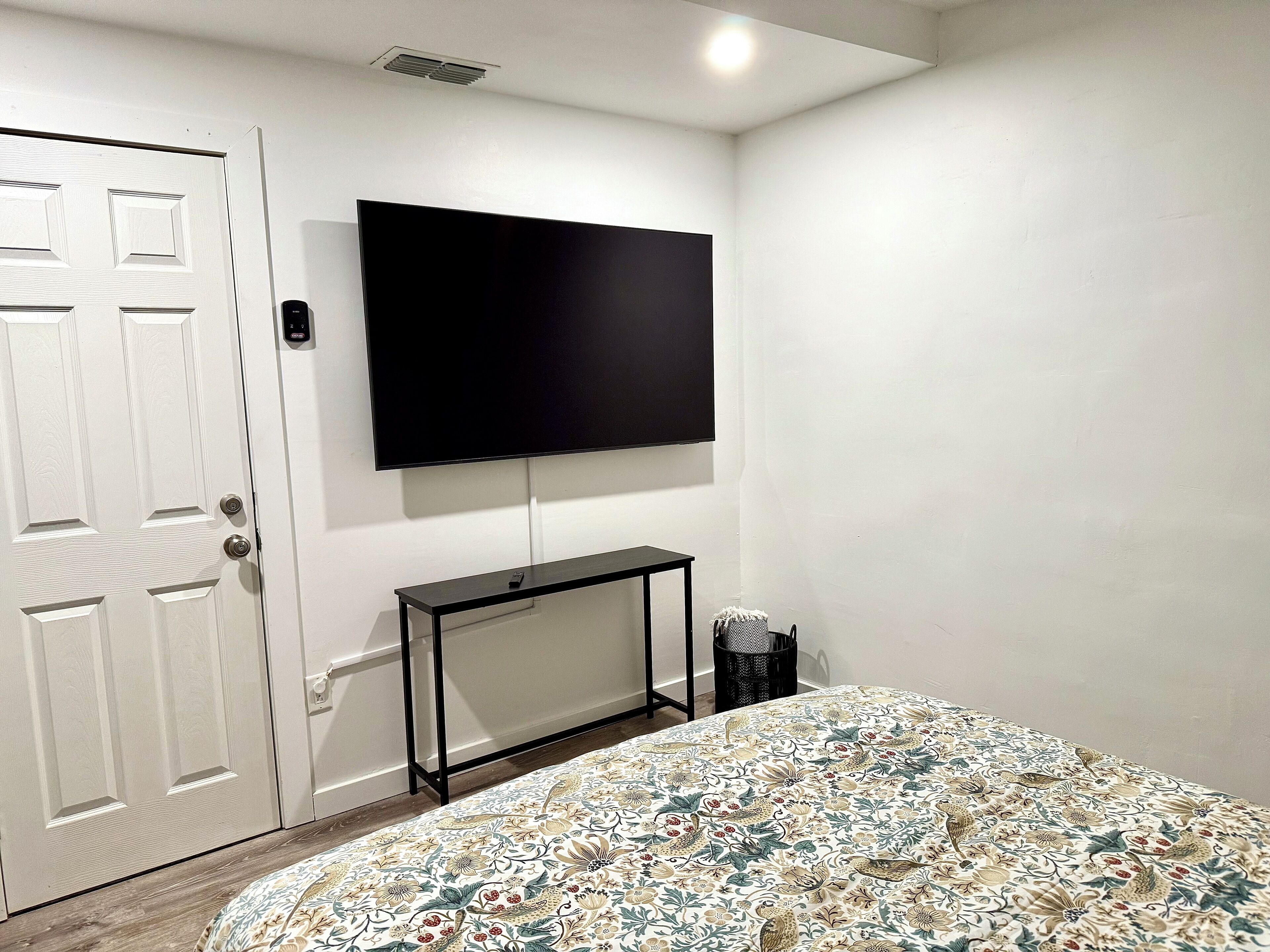 Une pièce comprenant un lit, un téléviseur fixé au mur, une porte et une petite table.