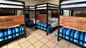 Een slaapzaal met stapelbedden, betegelde vloer en een enkele lamp aan het plafond.