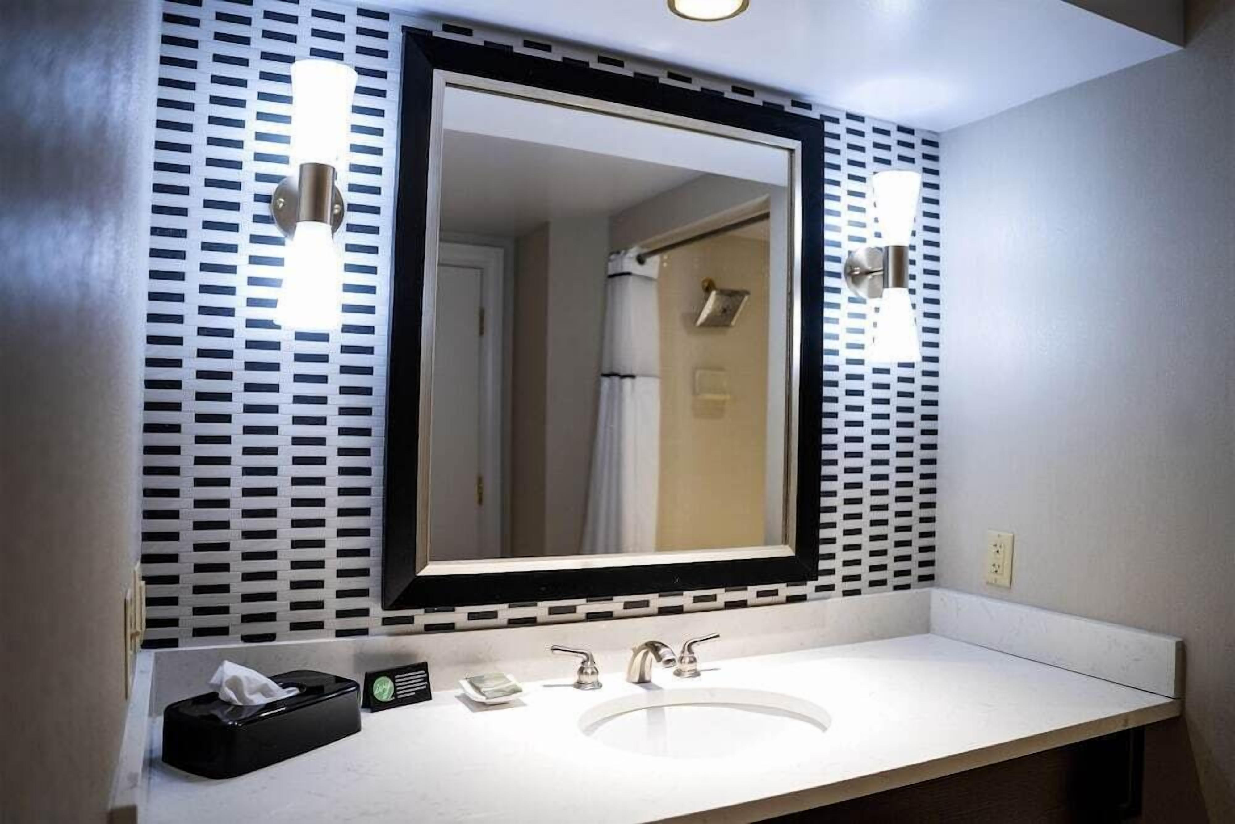 Een badkamer met een grote spiegel, een wastafel en twee wandlampen.