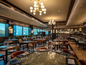 A restaurant with multiple dining tables and chairs, a bar area, and a view through large windows. - King Room at a  Hotel (Elizabeth)