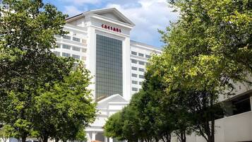 A modern hotel with a prominent 'Caesars' sign, surrounded by trees and a clear sky.