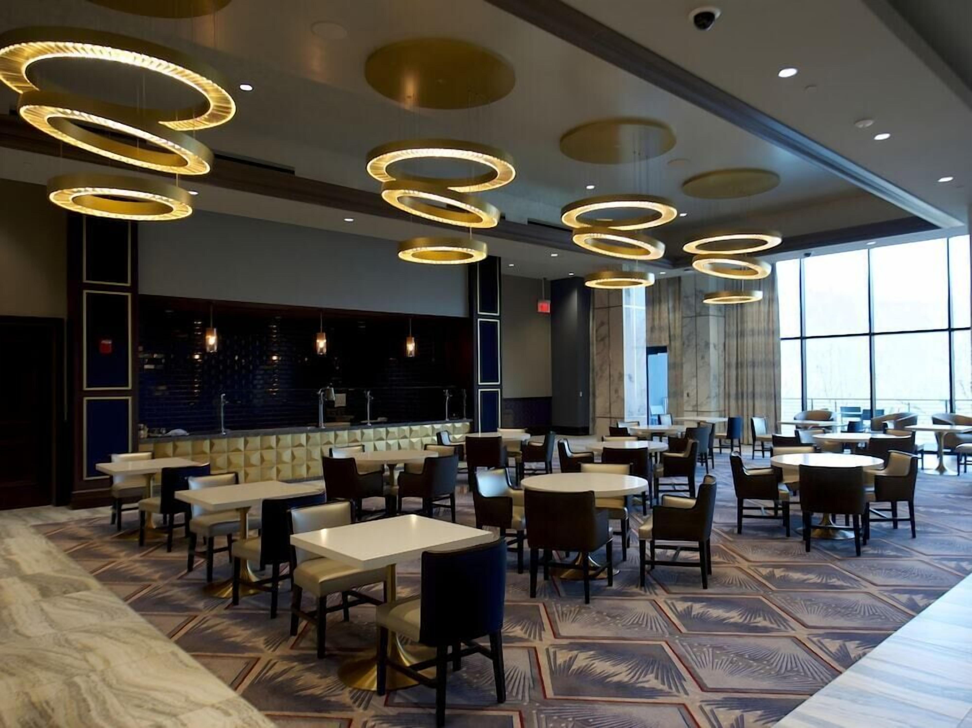 Un hall d’hôtel doté de plusieurs espaces salon, d’un bar et de grandes fenêtres.