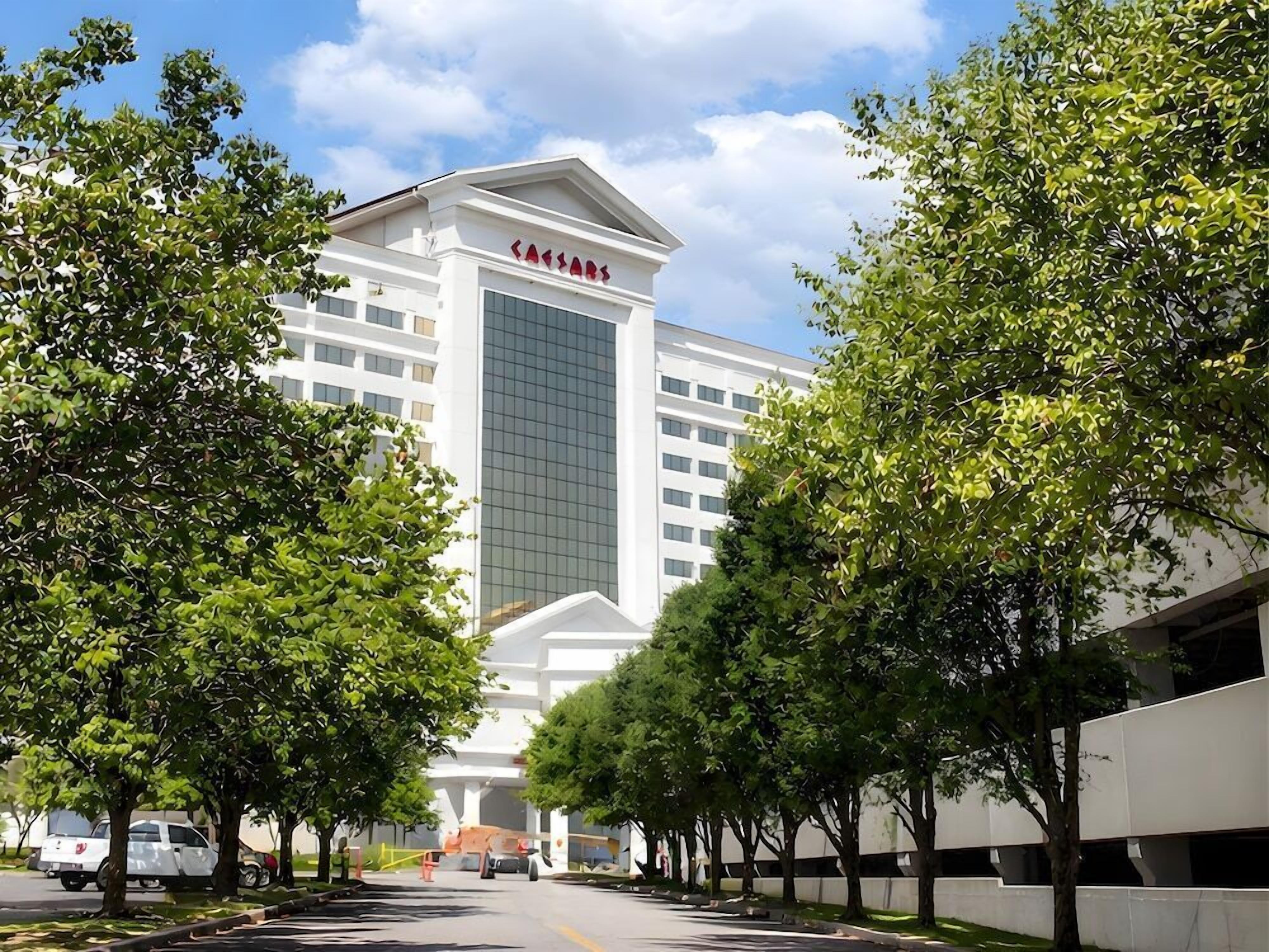 Ein modernes Hotel mit auffälligem 'Caesars'-Schild, umgeben von Bäumen und wolkenlosem Himmel.