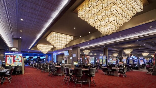 Un casino con varias mesas de juego y sillas, grandes candelabros y un letrero que indica 'No Fumar'.