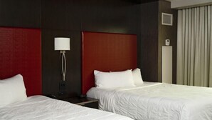 Habitación de hotel con dos camas, una pared de acento roja, una lámpara blanca y un ventanal con cortinas.