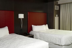Habitación de hotel con dos camas, una pared de acento roja, una lámpara blanca y un ventanal con cortinas.