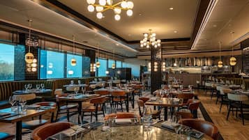 Un restaurante con varias mesas y sillas, una zona de bar y vistas amplias a través de grandes ventanales.