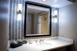 Un baño con un espejo grande, un lavamanos blanco y un bote de basura negro.