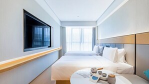 A hotel room with a large bed, a bedside table with a tea set, and a window with sheer curtains. - Full Season Hotel - PVG  (Shanghai)