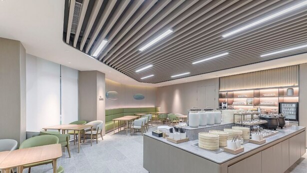 A modern cafe with a central island, seating area, and a counter with food items. - Full Season Hotel - PVG  (Shanghai)