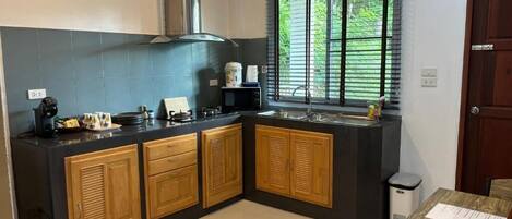 A compact kitchen with a black countertop, wooden cabinets, a built-in microwave, and a window with blinds.