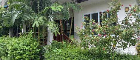 A house with a blue roof, surrounded by lush greenery including palm trees and flowering plants.