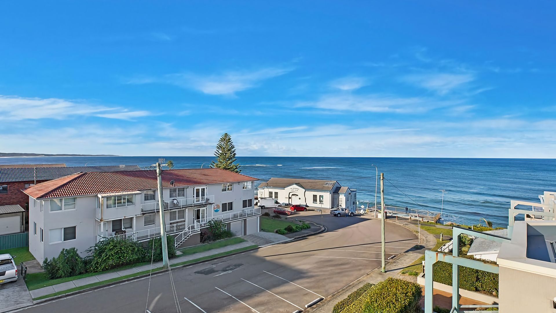 Ein Küstenwohngebiet mit freiem Blick auf das Meer, einem Parkplatz und einem Gebäude mit rotem Dach.