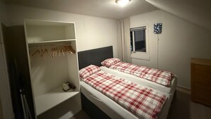 Pieni, hyvin valaistu makuuhuone, jossa on kaksi sänkyä, vaatekaappi ja ikkuna.