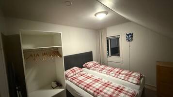 Une petite chambre bien éclairée, avec deux lits, une armoire et une fenêtre.