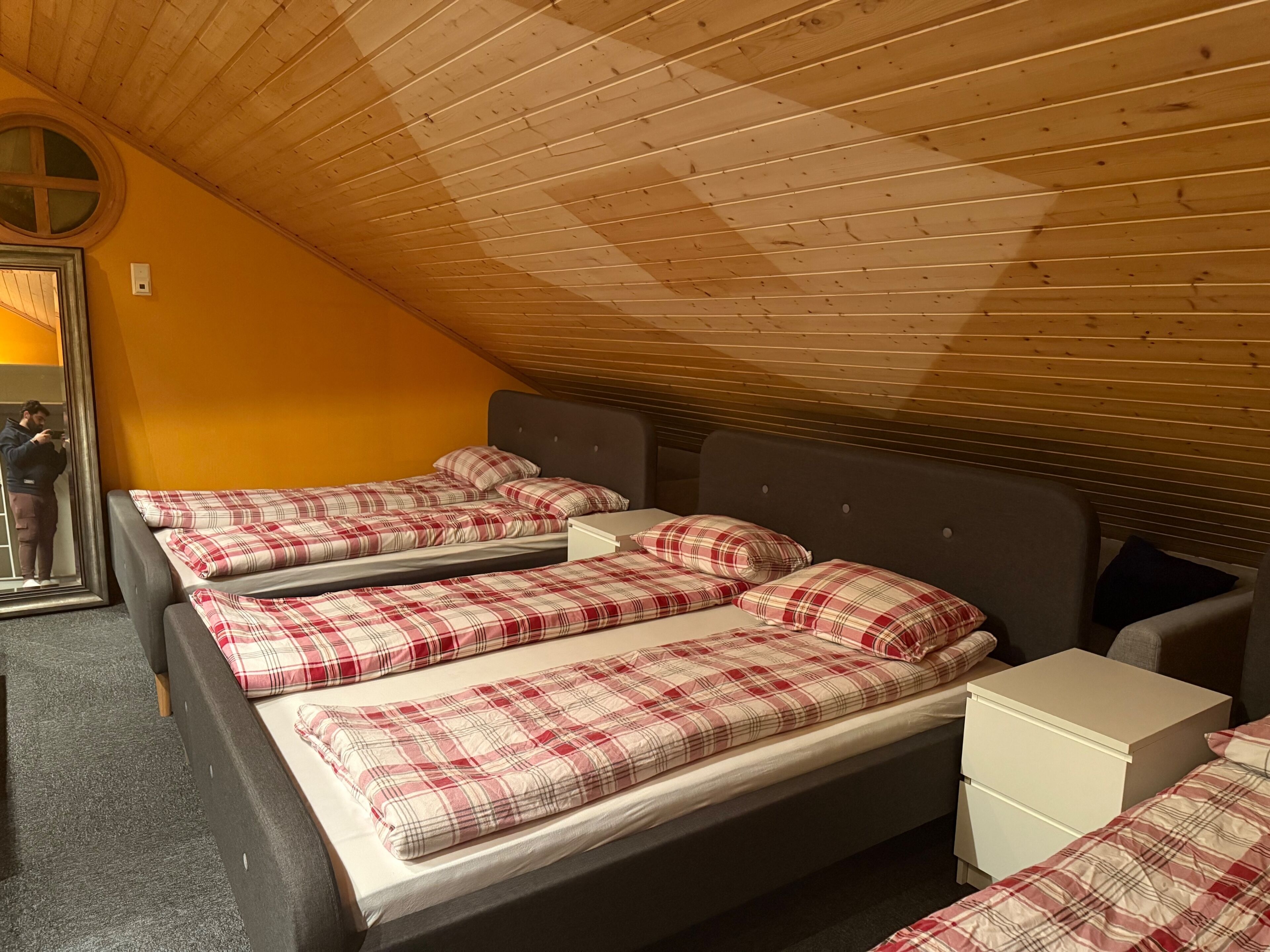 Una habitación con tres camas, cada una con ropa de cama escocesa, techo de madera y pared amarilla.