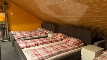 Una habitación con tres camas, cada una con ropa de cama escocesa, techo de madera y pared amarilla.