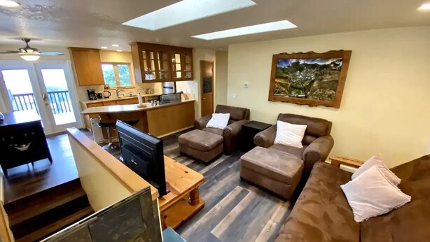 A modern living room with a sofa set, a television, and a kitchen area with wooden cabinets and a dining table. - Charming 2-bedroom apartment with AC in Rainier (Rainier)