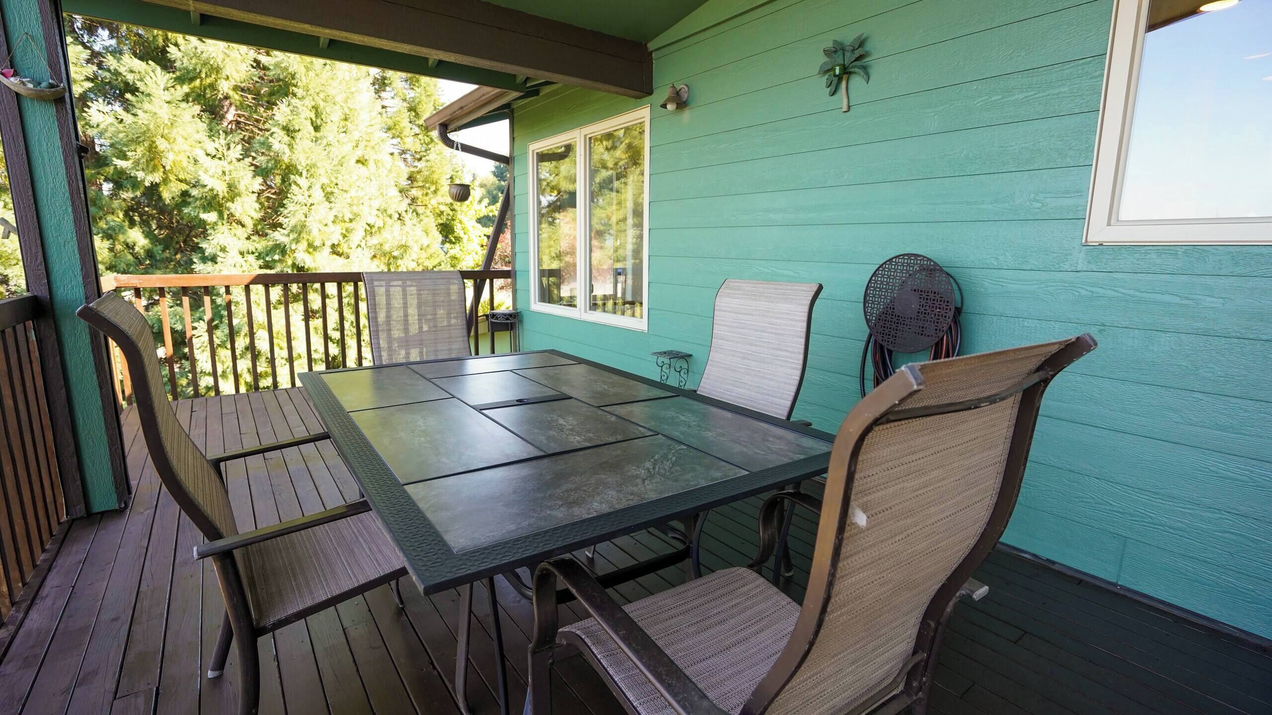 Un espace extérieur abrité, aménagé pour prendre les repas, avec une table et des chaises, un petit ventilateur et une fenêtre donnant sur les arbres.