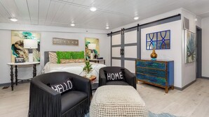A modern bedroom with a bed, two chairs, a dresser, and artwork on the walls.