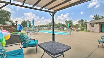 An outdoor pool area with lounge chairs and umbrellas, a covered seating area, and a small building.