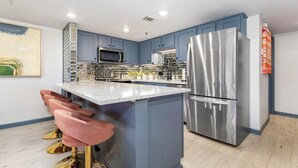 A modern kitchen with blue cabinets, stainless steel appliances, and a central island with bar stools.