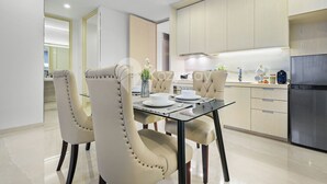 A modern kitchen with light wood cabinets, a stainless steel refrigerator, and a dining area with a glass table and cushioned chairs.