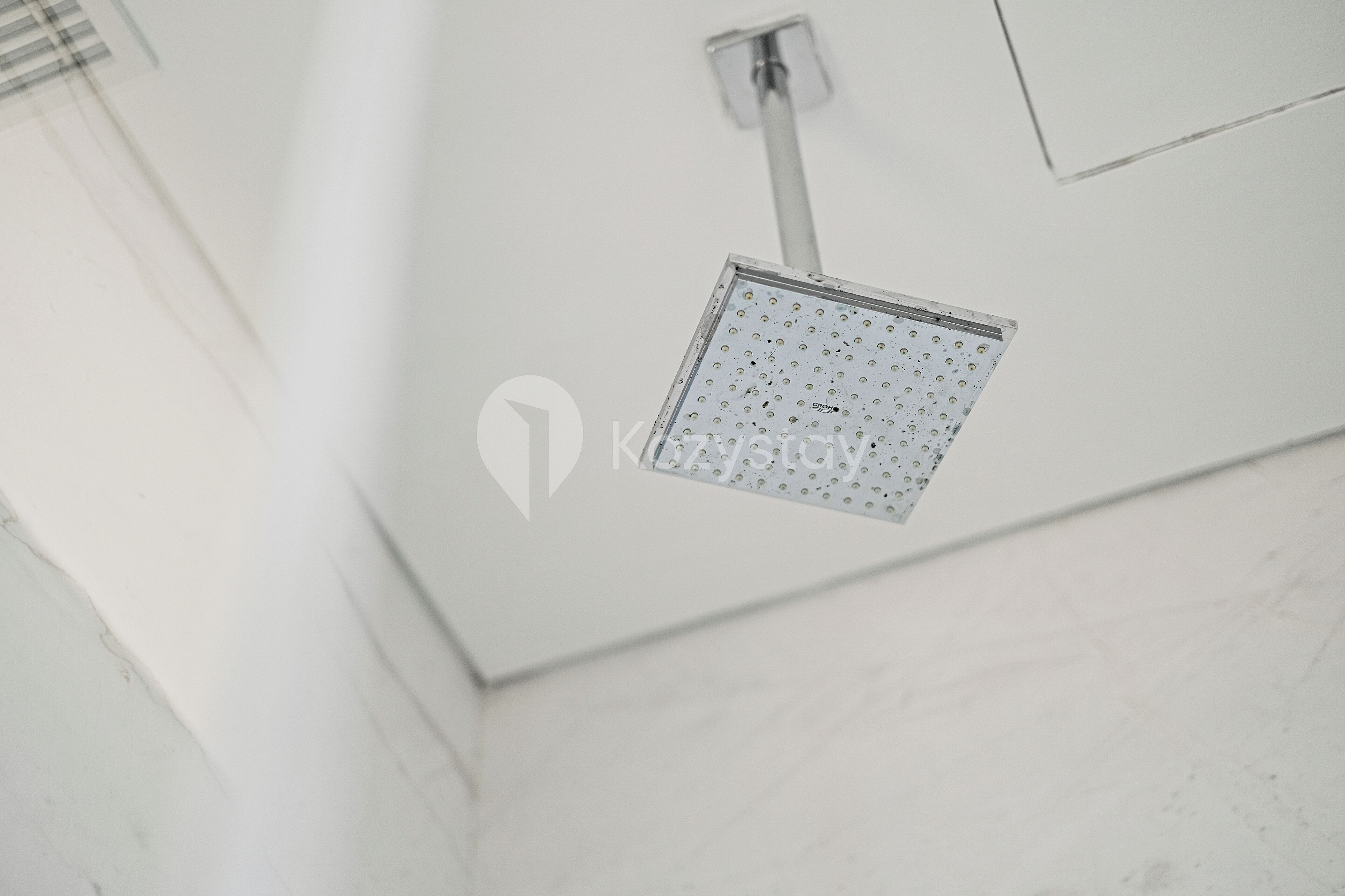 A ceiling-mounted showerhead in a bathroom with white walls and a visible pipe.