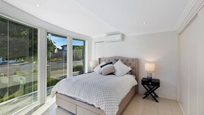 A modern bedroom with a large bed, a nightstand, a lamp, and a view through floor-to-ceiling windows. - Skywaters Retreat 2 Bedroom (The Entrance)