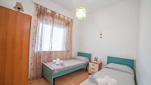 Un dormitorio con dos camas, una ventana con cortinas, una mesita de noche con lámpara y un armario.