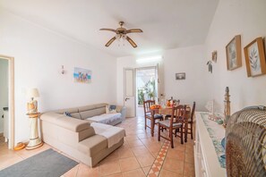 Una sala de estar con sofá, una mesa de comedor con sillas, un ventilador de techo y una puerta que da al exterior.