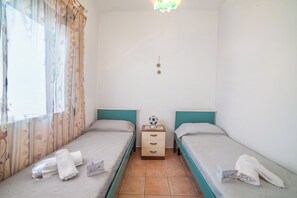 A small, clean room with two single beds, a bedside table with a lamp, and a window with curtains. - Rusciu Te Lu Mare Apartment with Terrace & Garden, Porto Cesareo, Italy (Porto Cesareo)