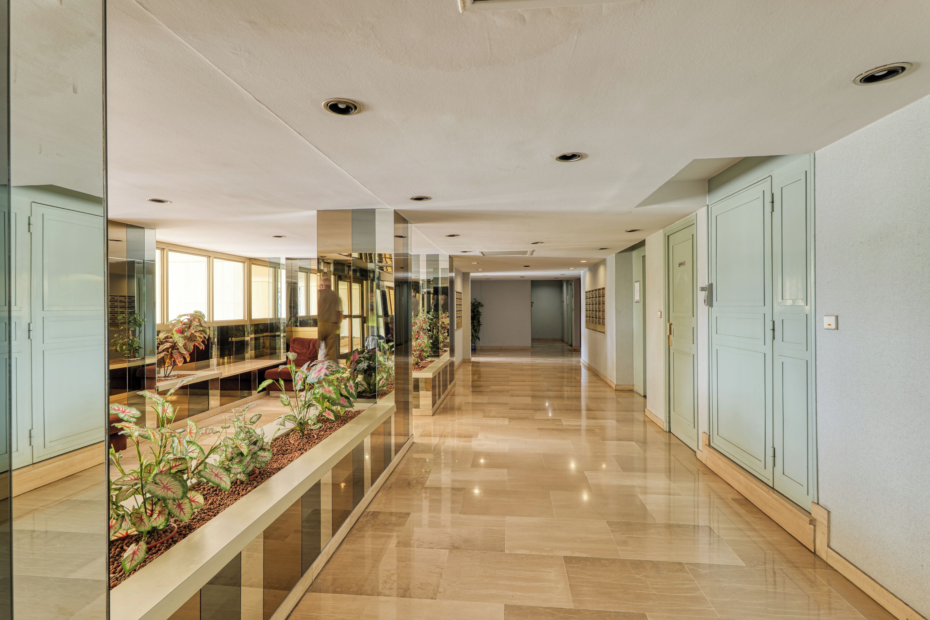 Corredor moderno de hotel com guarda-corpos de vidro, plantas em vasos e piso lustroso.