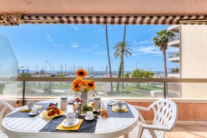 A balcony with a table set for breakfast, overlooking a marina and palm trees.