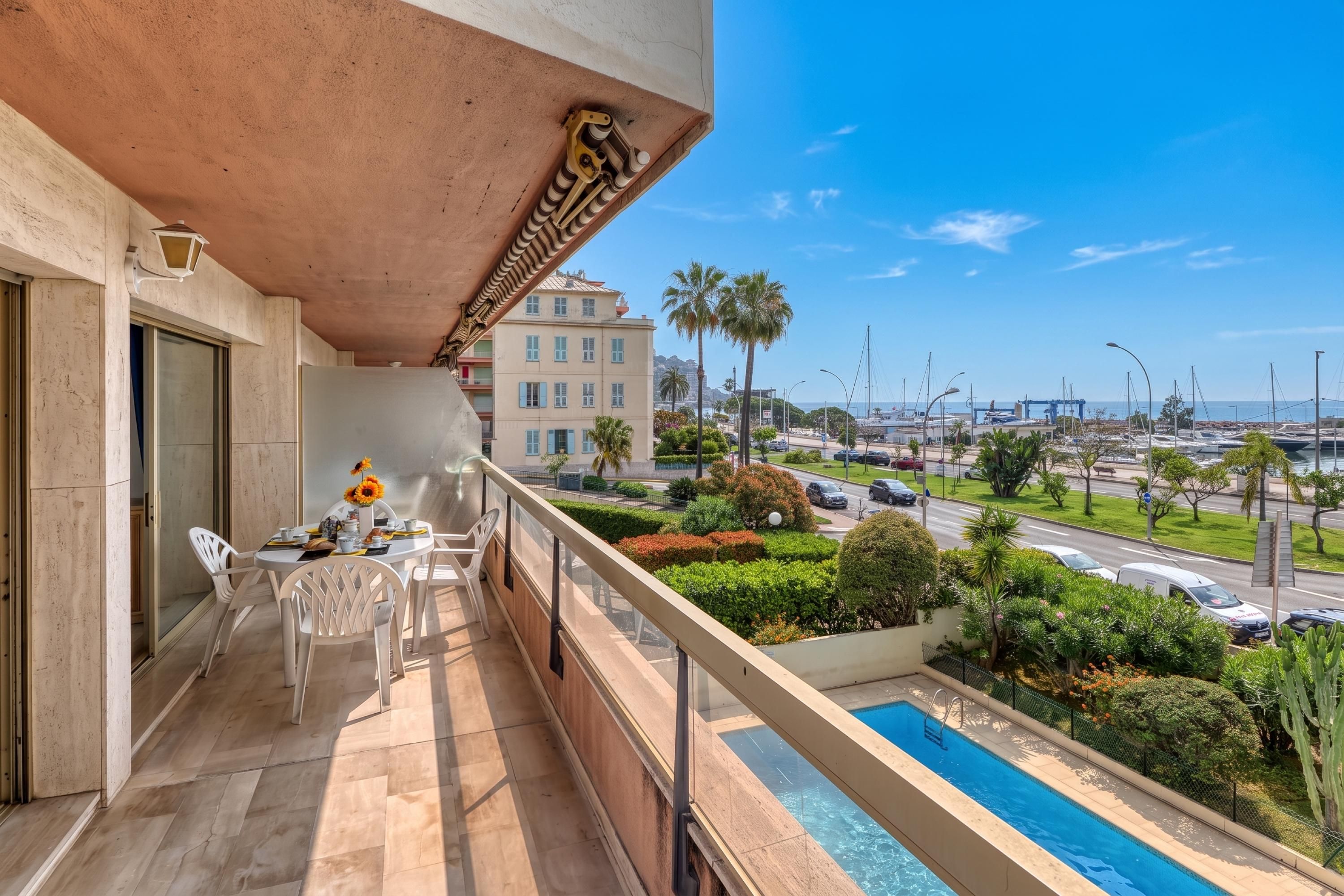 A balcony with a pool, chairs, and a dining table with sunflowers.