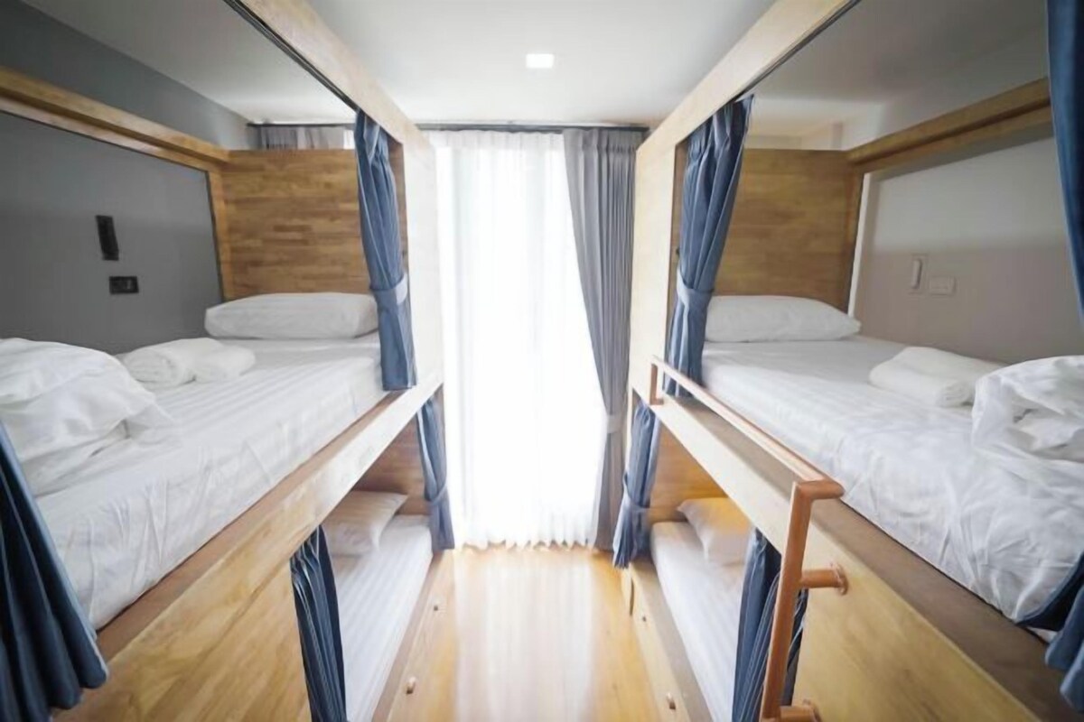 A compact room with two bunk beds, wooden headboards, and a small window with curtains.