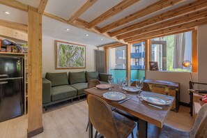 A dining area with a wooden table set for four, a sofa, and a refrigerator. - Résidence Grand Roc - Bruyères 221, Argentière (Chamonix), France (Argentière (Chamonix))